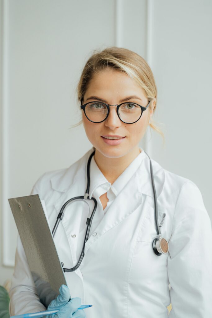 pexels photo 5215024 5215024 Smiling female healthcare professional in white coat holding clipboard indoors.